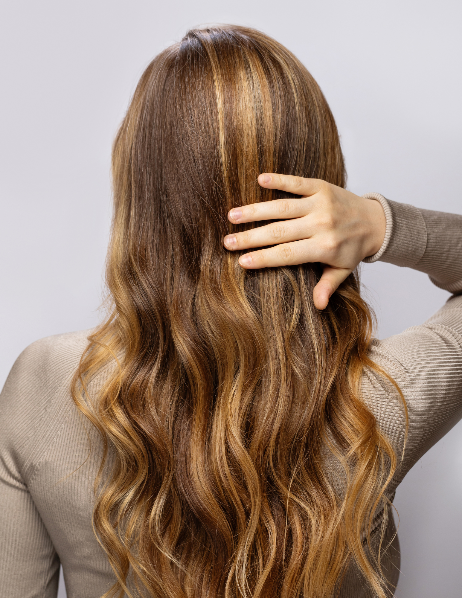 A woman is touching her long brown hair with her hand.