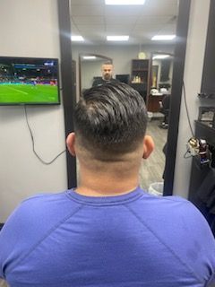 A man is sitting in front of a mirror in a barber shop.