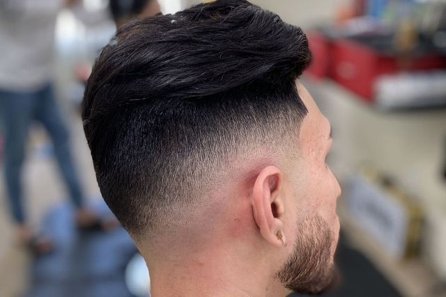 A man with a beard is getting his hair cut at a barber shop.