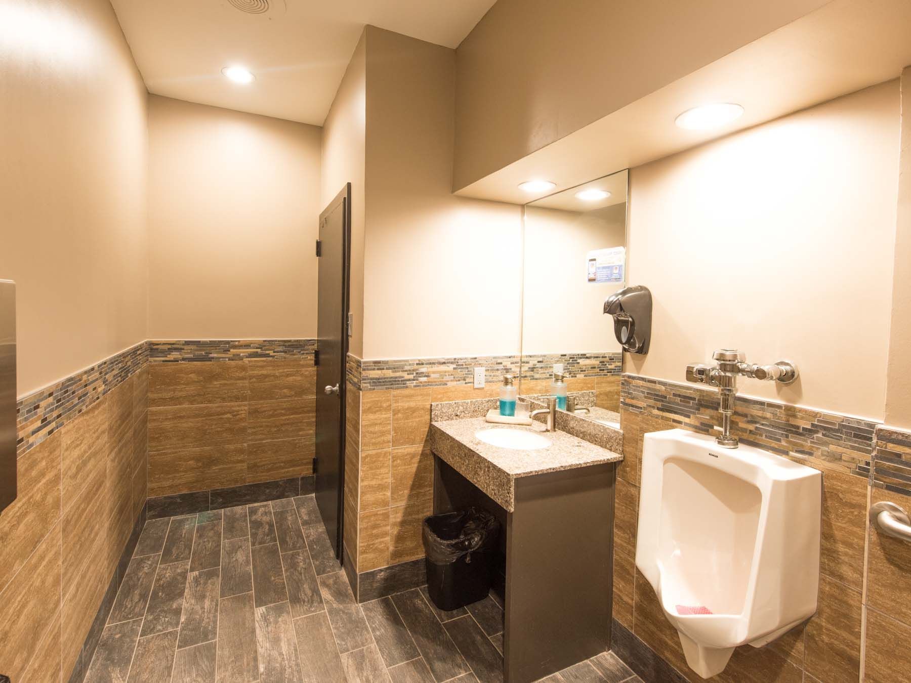 A bathroom with a urinal , sink and mirror.