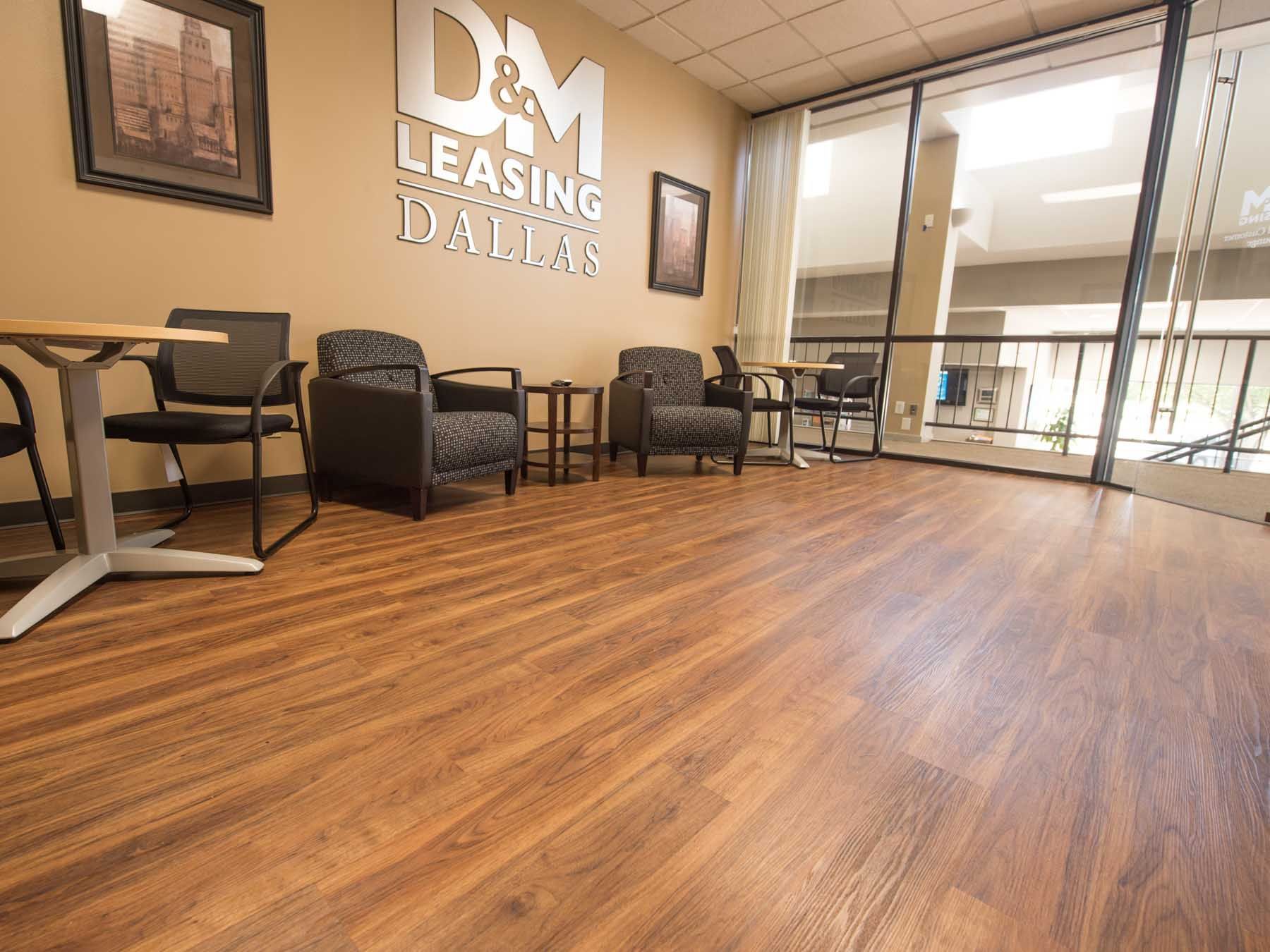 A waiting room with wooden floors , chairs , tables and a large window.