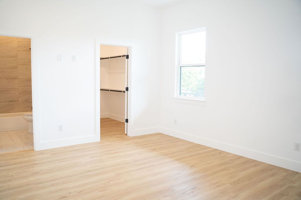 Empty, bright bedroom with light wooden floors and a closet visible through an open door. A window is on the right.