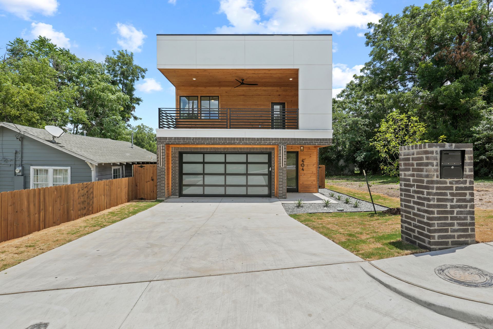 Modern two-story house with a white upper level, wooden accents, and a glass garage door.