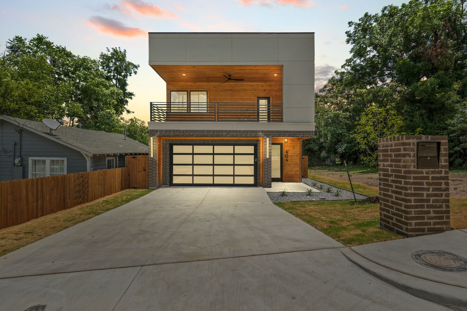 Modern two-story home with a white upper level, garage, and balcony; a concrete driveway leads to the entrance.