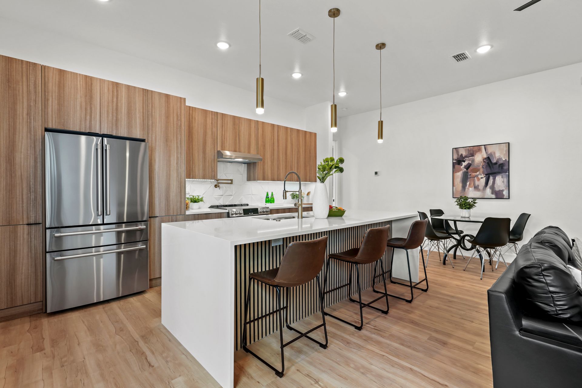 Modern kitchen with wood cabinets, stainless steel appliances, island with bar stools, and dining area.