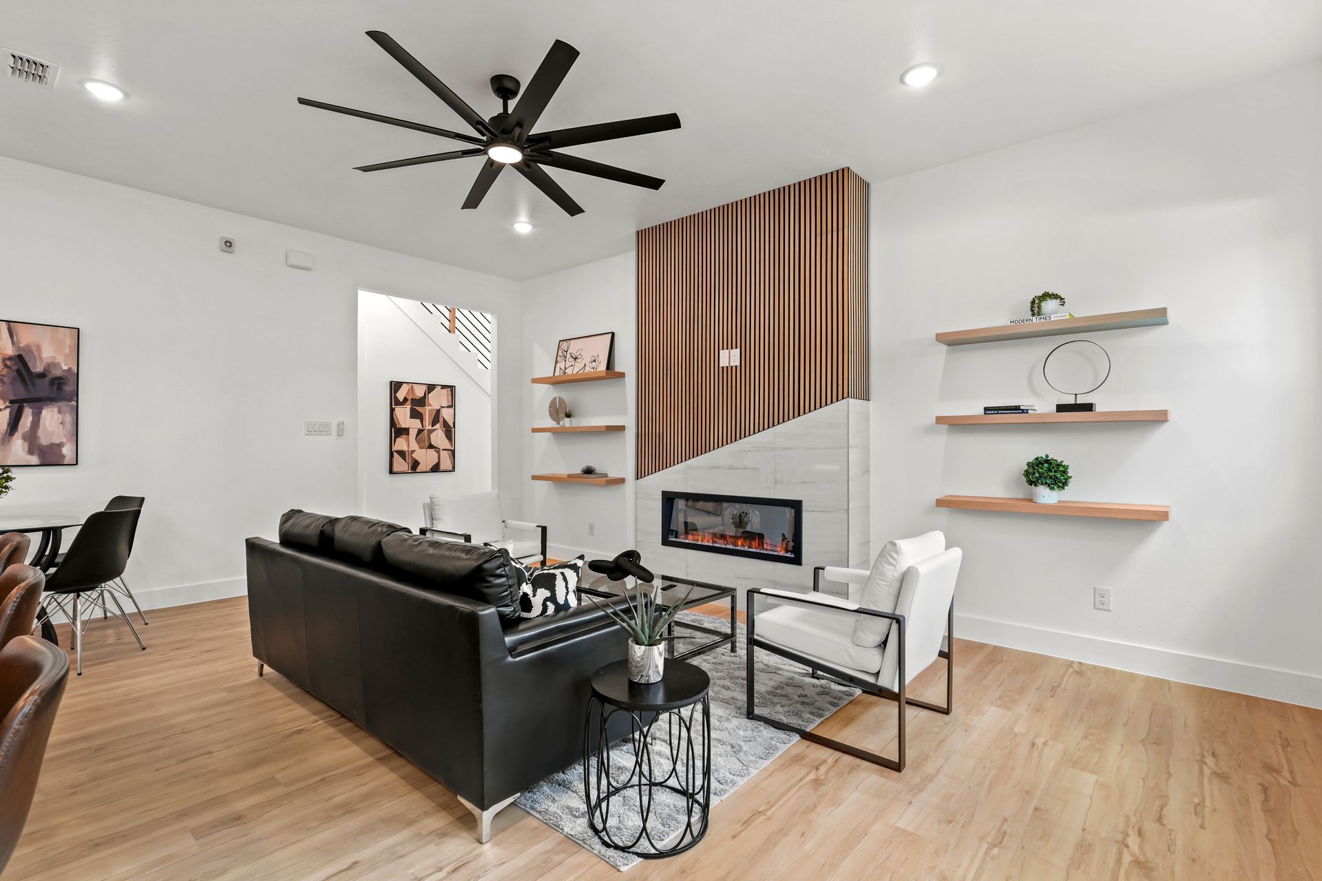 Modern living room with white walls, hardwood floors, black leather sofa, and fireplace.