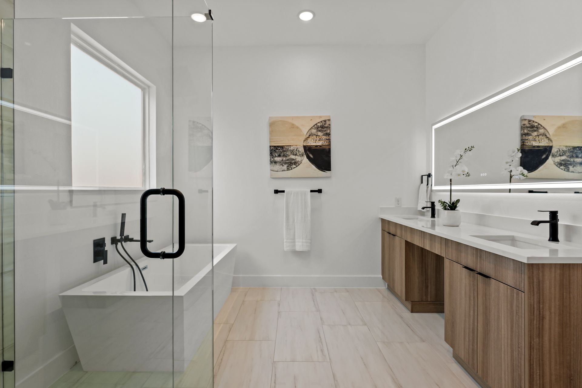 Modern bathroom with a freestanding tub, glass shower, double vanity with wood cabinets, and abstract art.