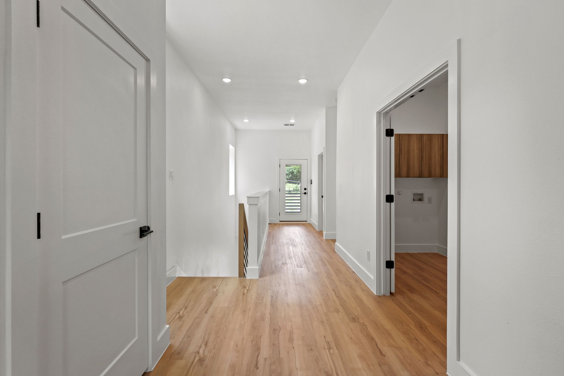 Hallway with wood floors, white walls and doors, and a view to a door with light shining through