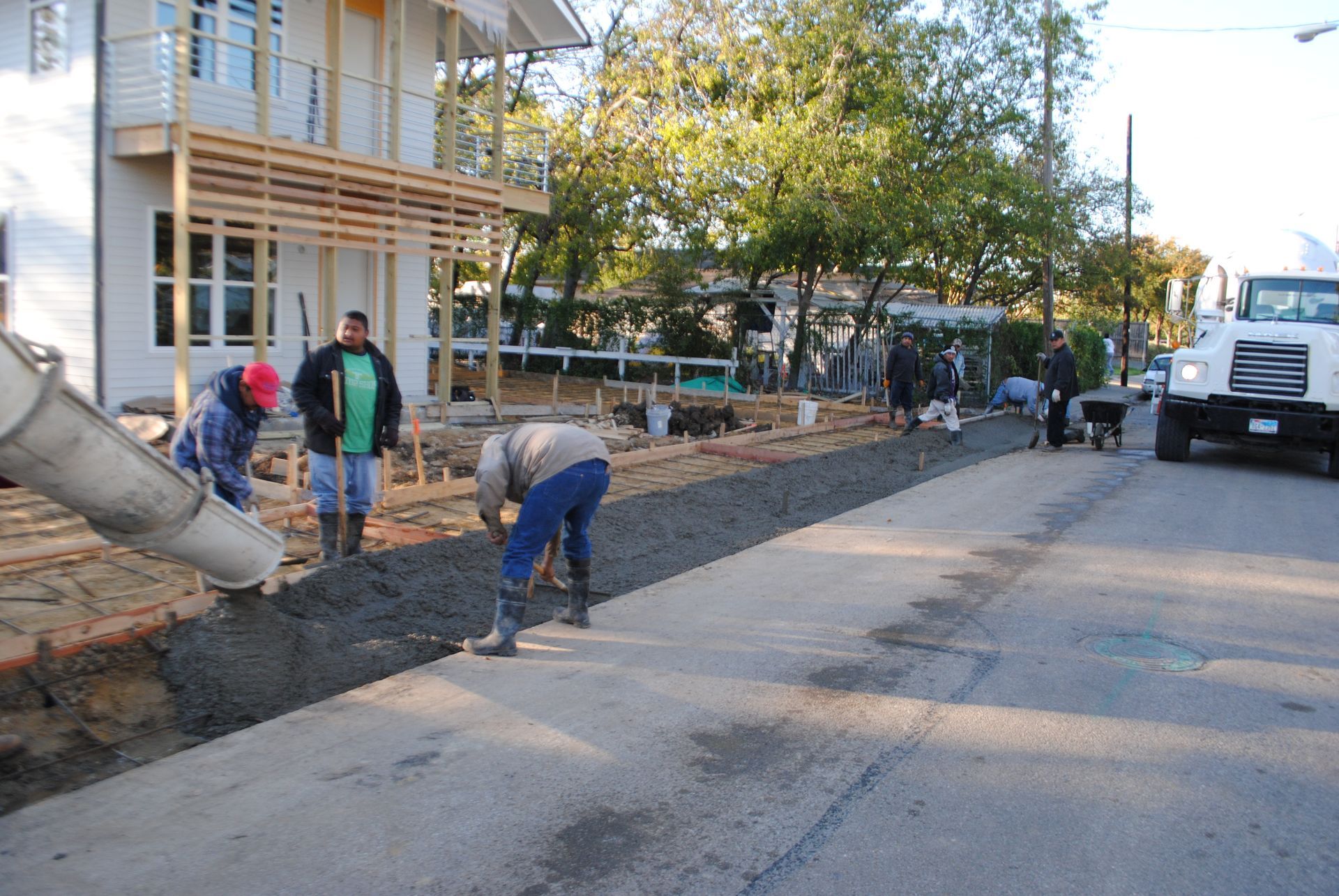 A truck is pouring concrete on a sidewalk in front of a house