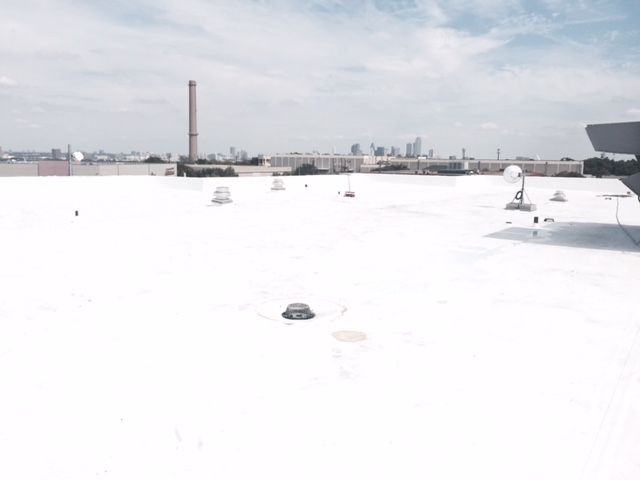 A white roof with a chimney in the background and a city skyline in the background.