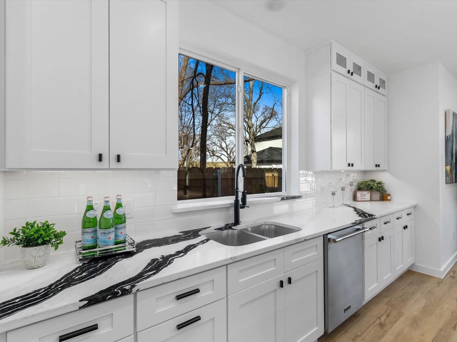 A modern kitchen with white cabinets, black countertops, stainless steel appliances, and a window with a view of trees.