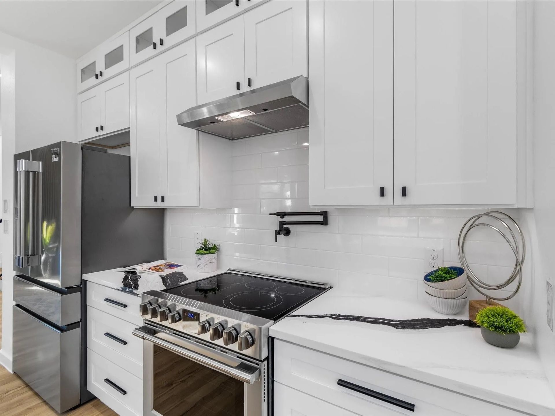 White kitchen with stainless steel appliances, white cabinets, and a black cooktop.