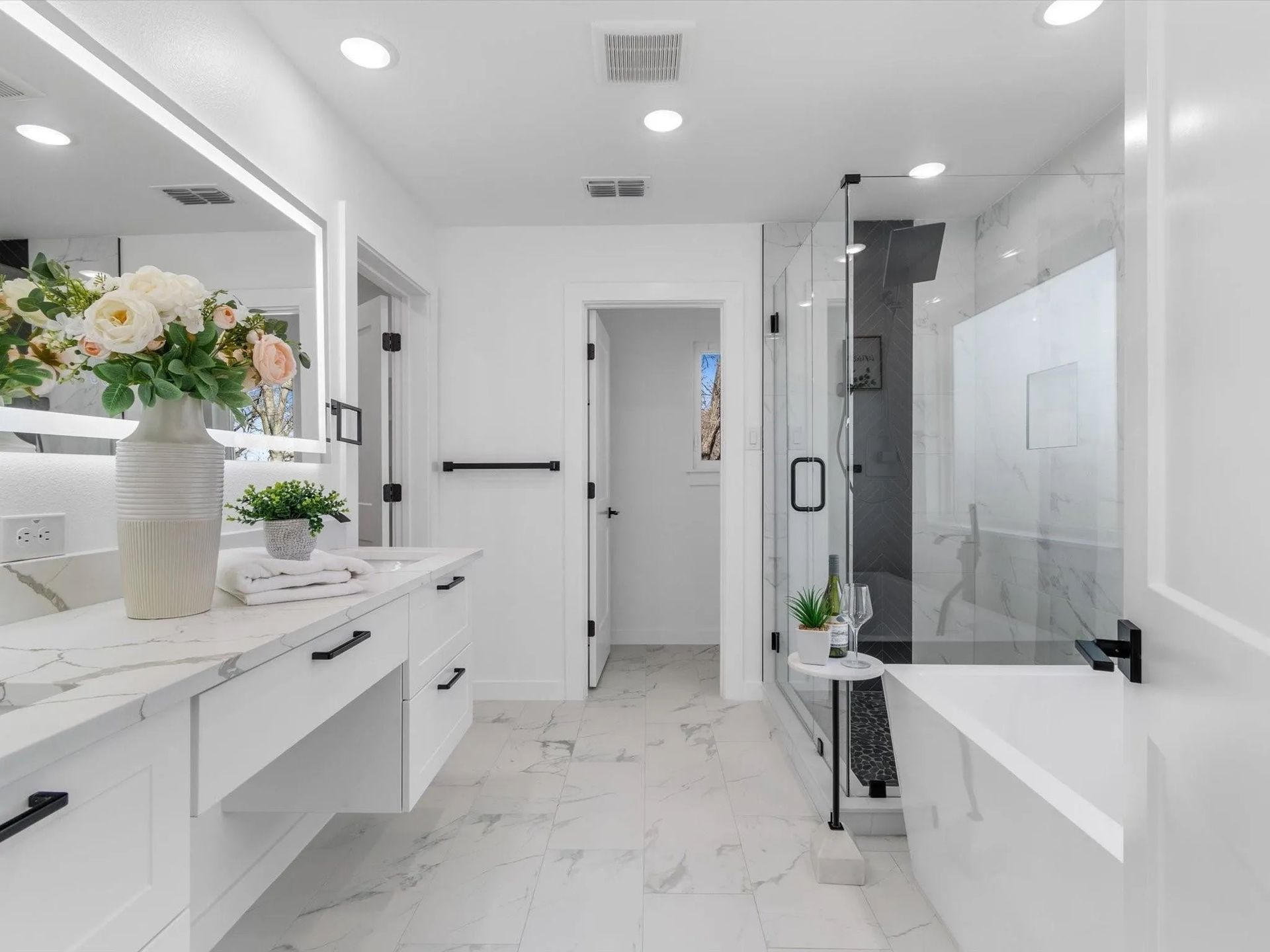 White bathroom with marble floors and countertops, a glass shower, and a freestanding tub.
