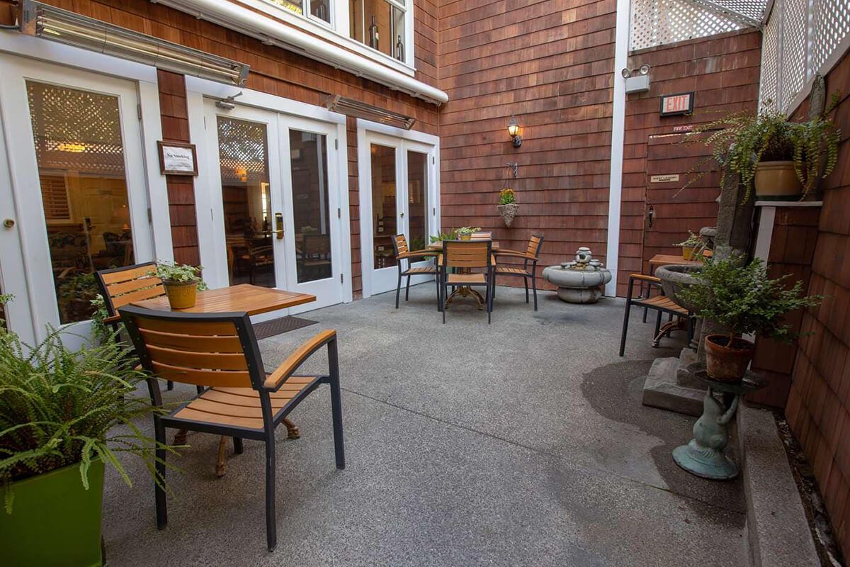 Patio with brown shingle siding, tables, chairs, and potted plants.