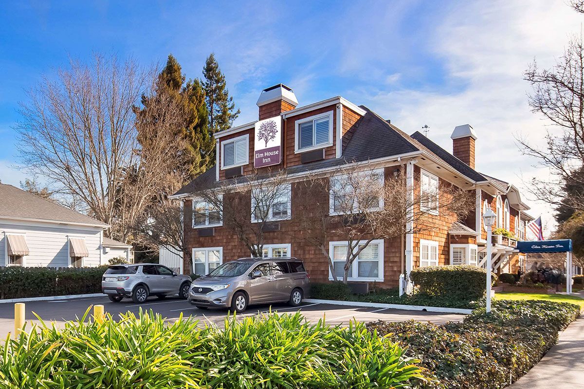 Two-story brick building with cars parked out front, a sign with a tree logo, and a blue sky.