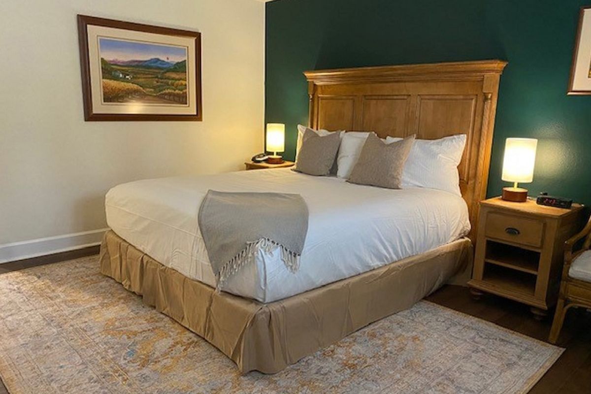 Bedroom with queen-size bed, beige bedding, nightstands, lamps, artwork, and area rug. Green and beige walls.