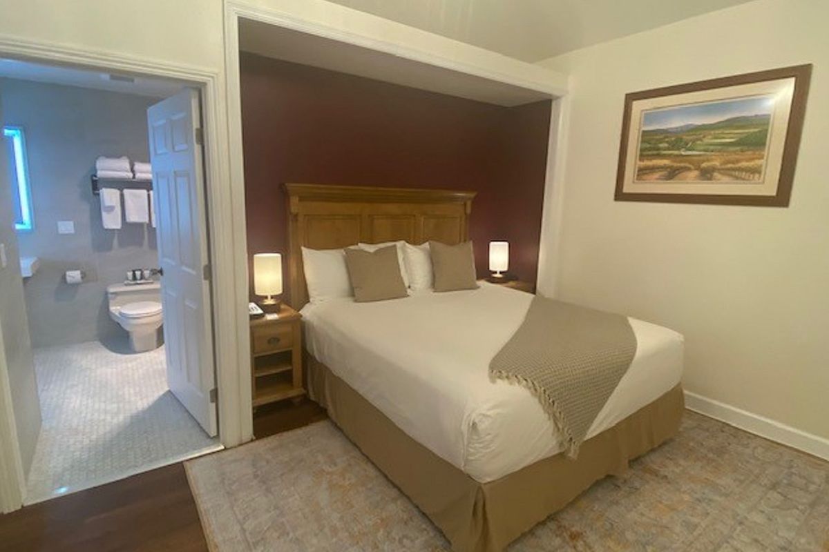 Bedroom with a bed, bedside tables, and an open doorway to a bathroom. The wall behind the bed is burgundy.