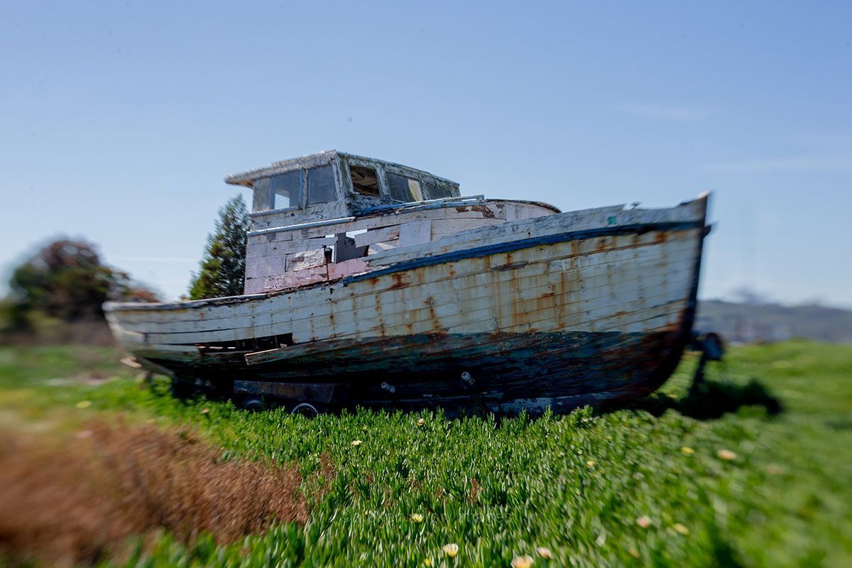 Dilapidated boat on grassy land under a bright blue sky.