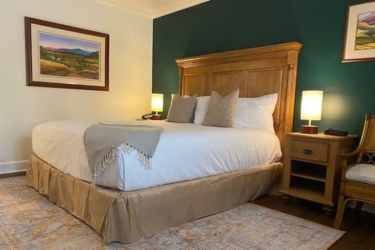 Bedroom with large wooden headboard, queen bed with white linens, two lamps on nightstands, green accent wall, and artwork.