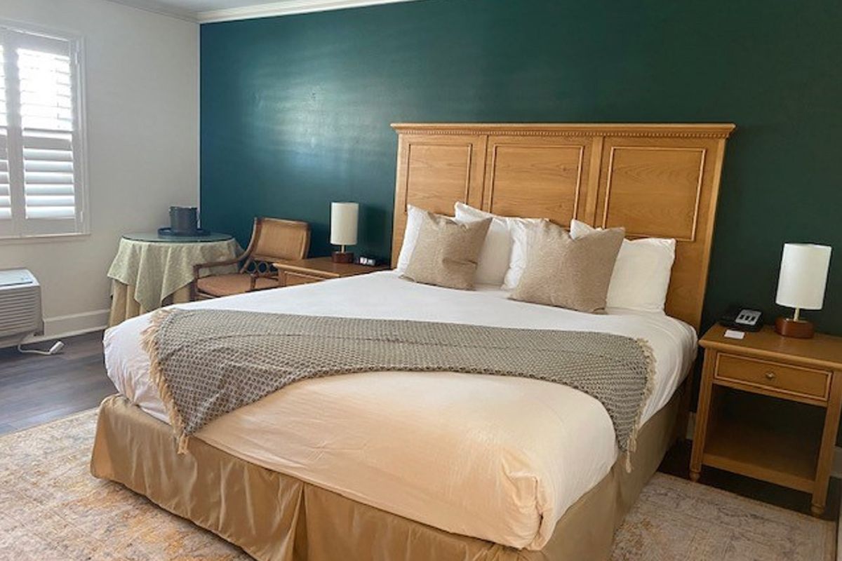 Hotel bedroom with a bed, nightstands, and a desk against a dark green wall.