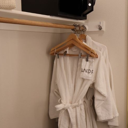 White bathrobes hanging in a closet, with a wooden rod and a small safe above.