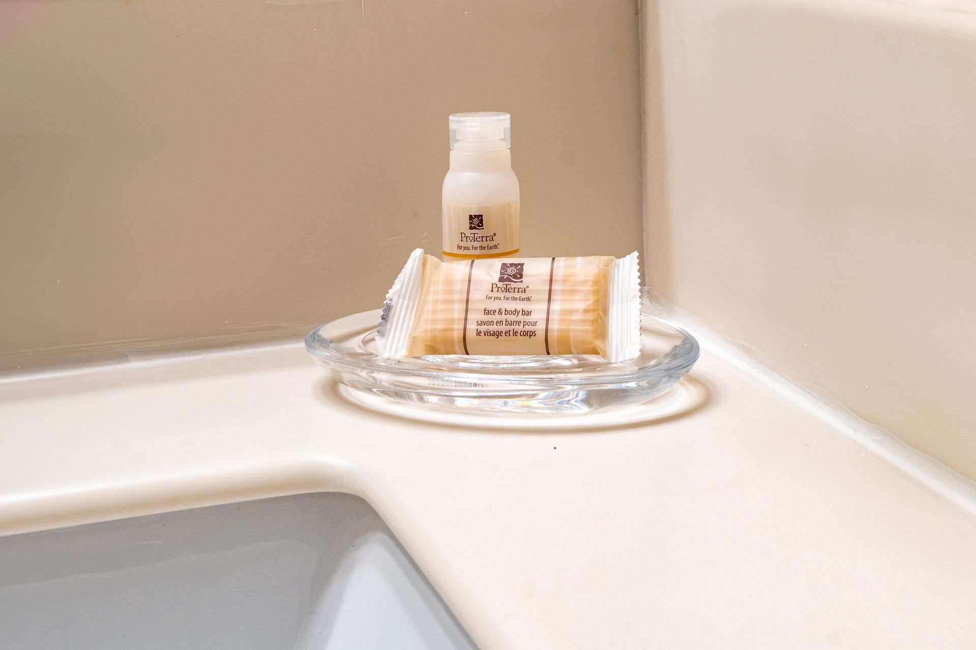 Soap and lotion bottles on a clear glass soap dish in a bathroom corner.