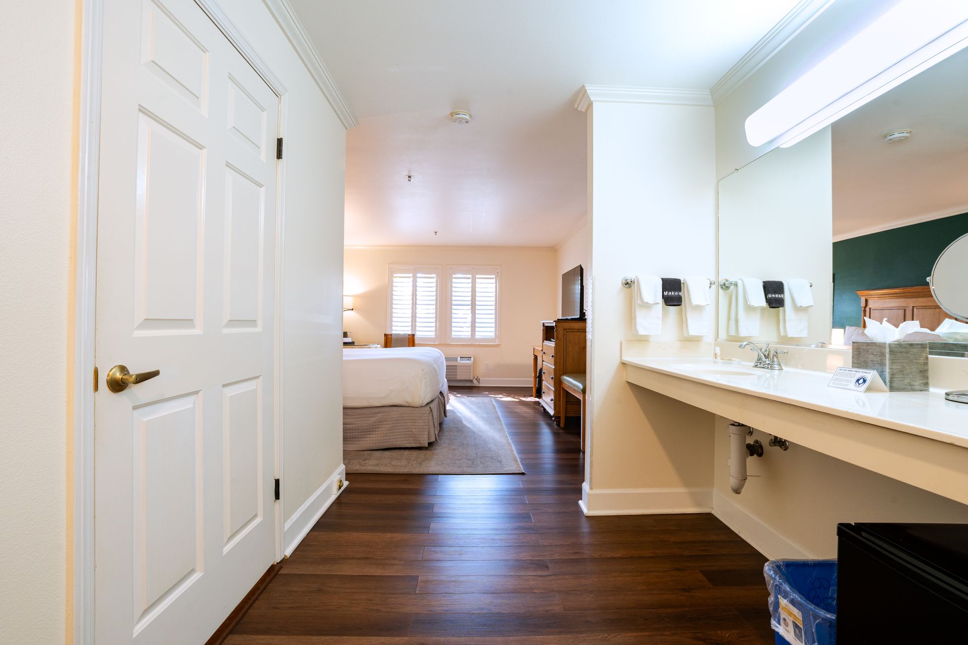 Hotel room with hardwood floor, bed, bathroom vanity, and closed door.