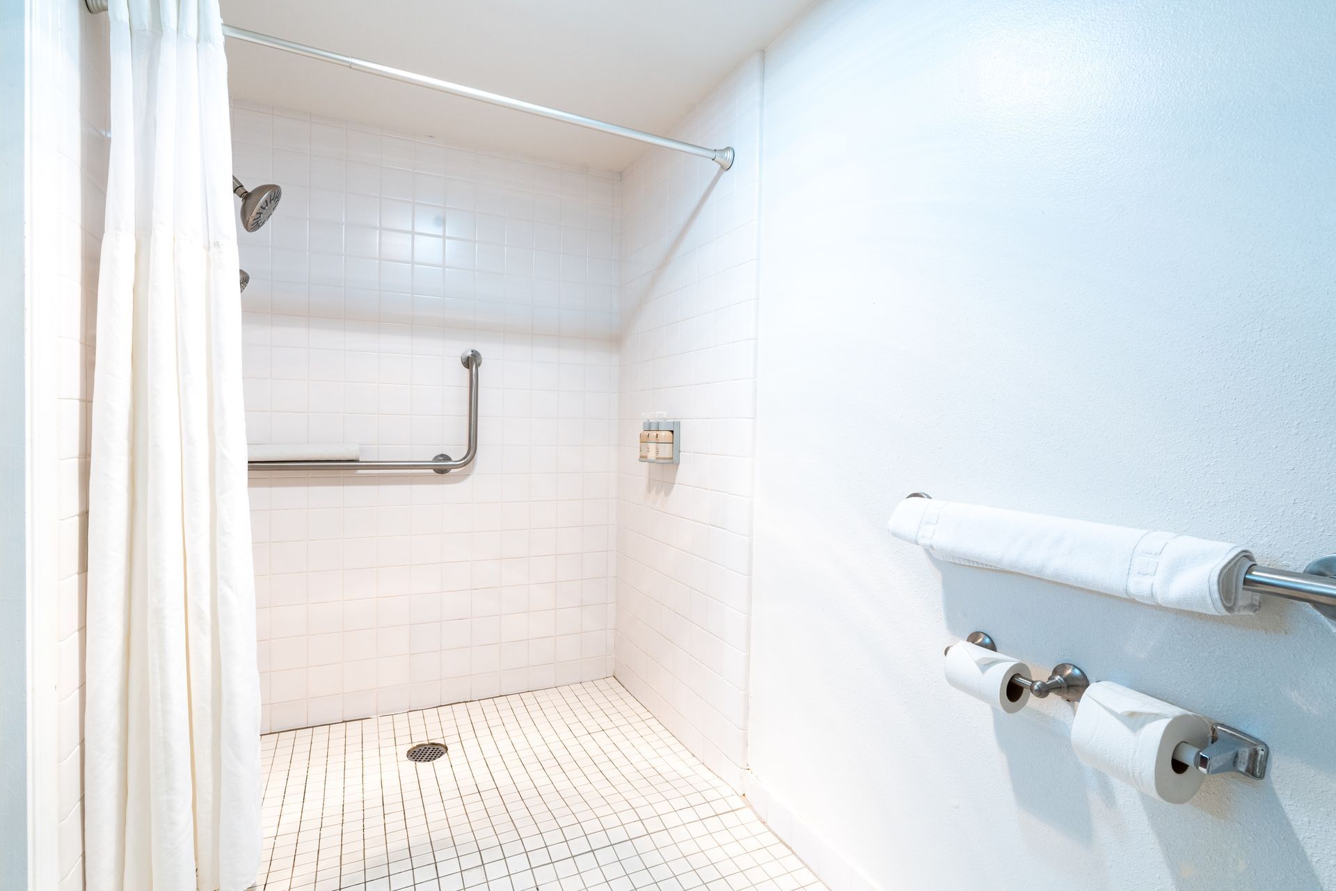 White-tiled shower with grab bars and a curtain rod.