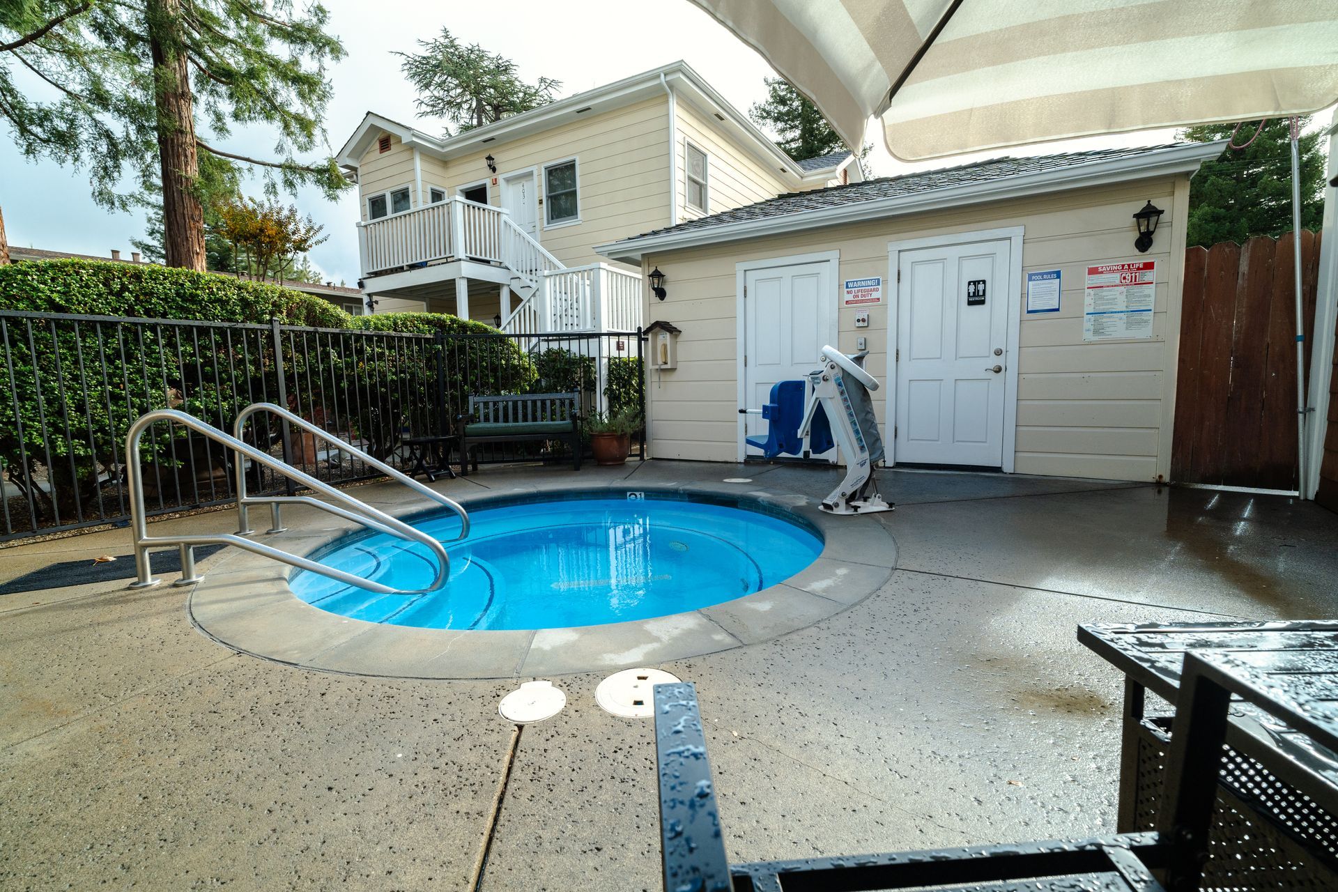 Hot tub surrounded by concrete patio, small building, and a two-story building in the background.
