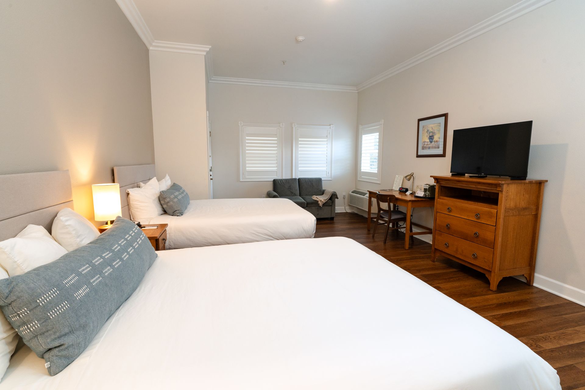A hotel room with two queen beds, a dresser, desk, and small sofa.