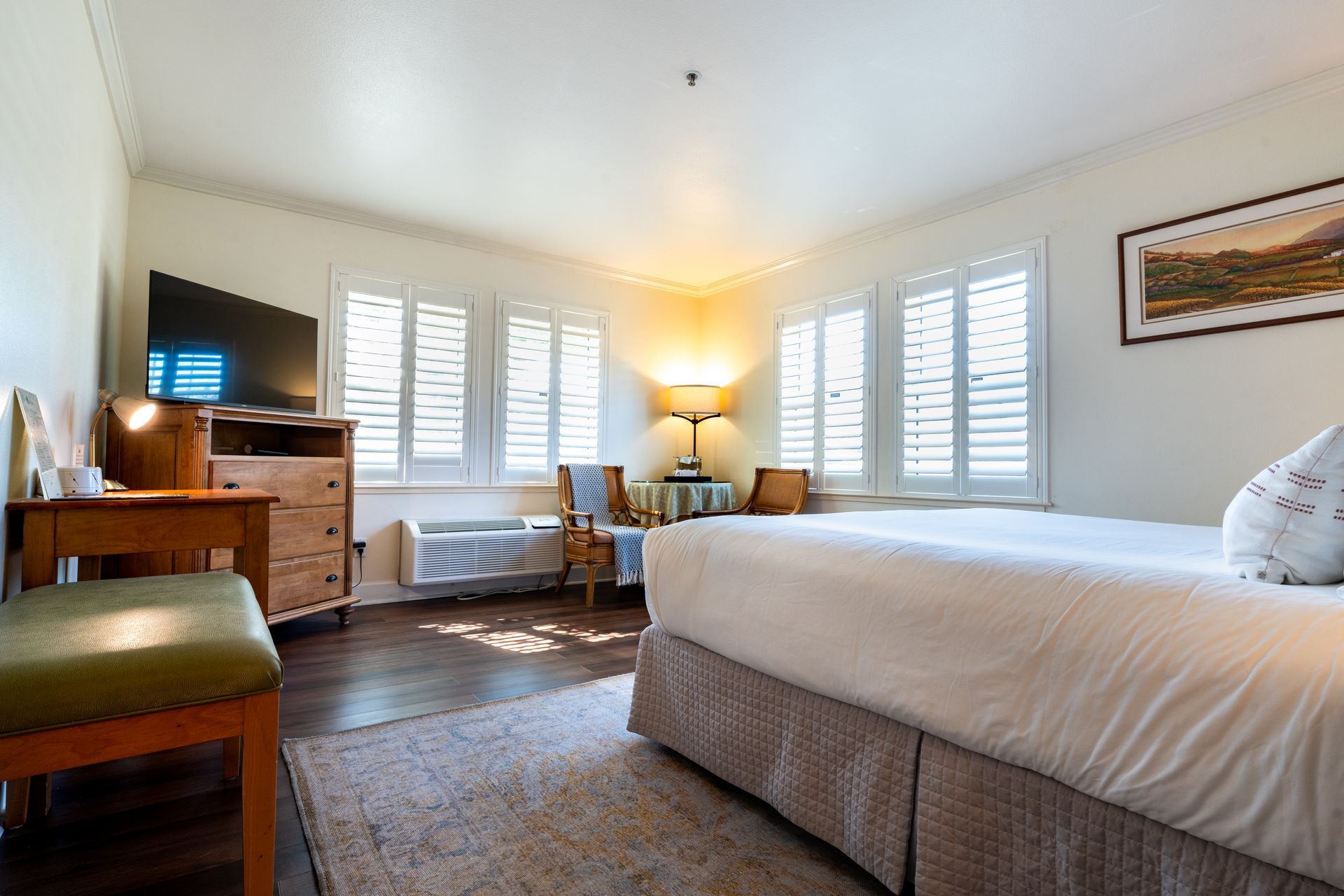 Bedroom with bed, dresser, table, chairs, windows with shutters, and rug.