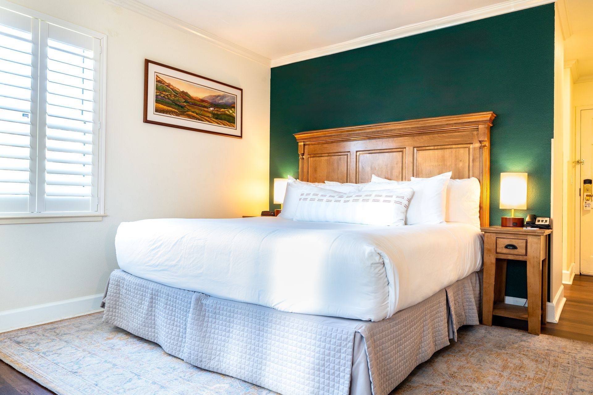 Bedroom with king bed, teal accent wall, wooden headboard, shutters, nightstand, and rug.