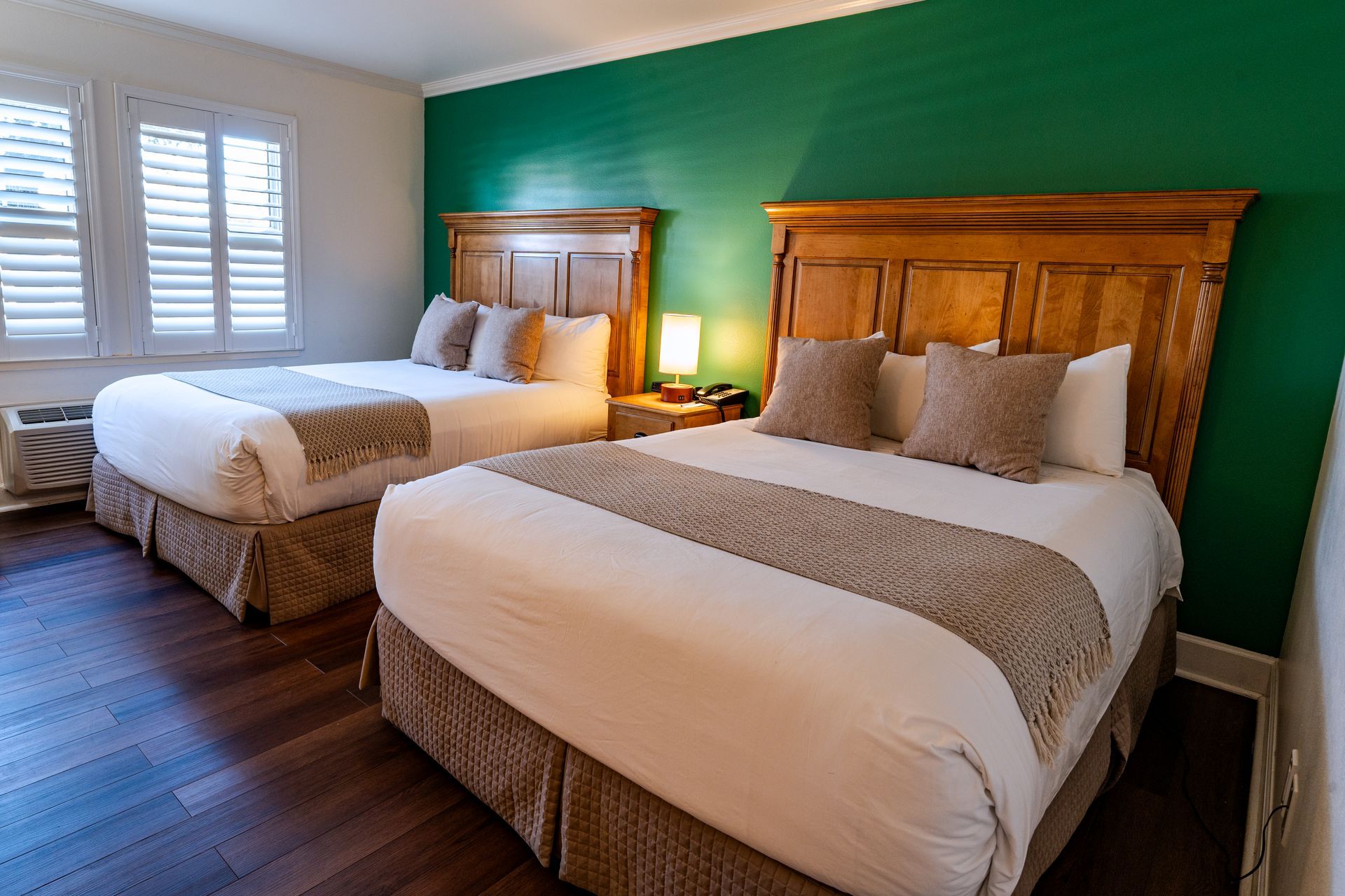 Two queen beds in a hotel room with green wall and wooden headboards.