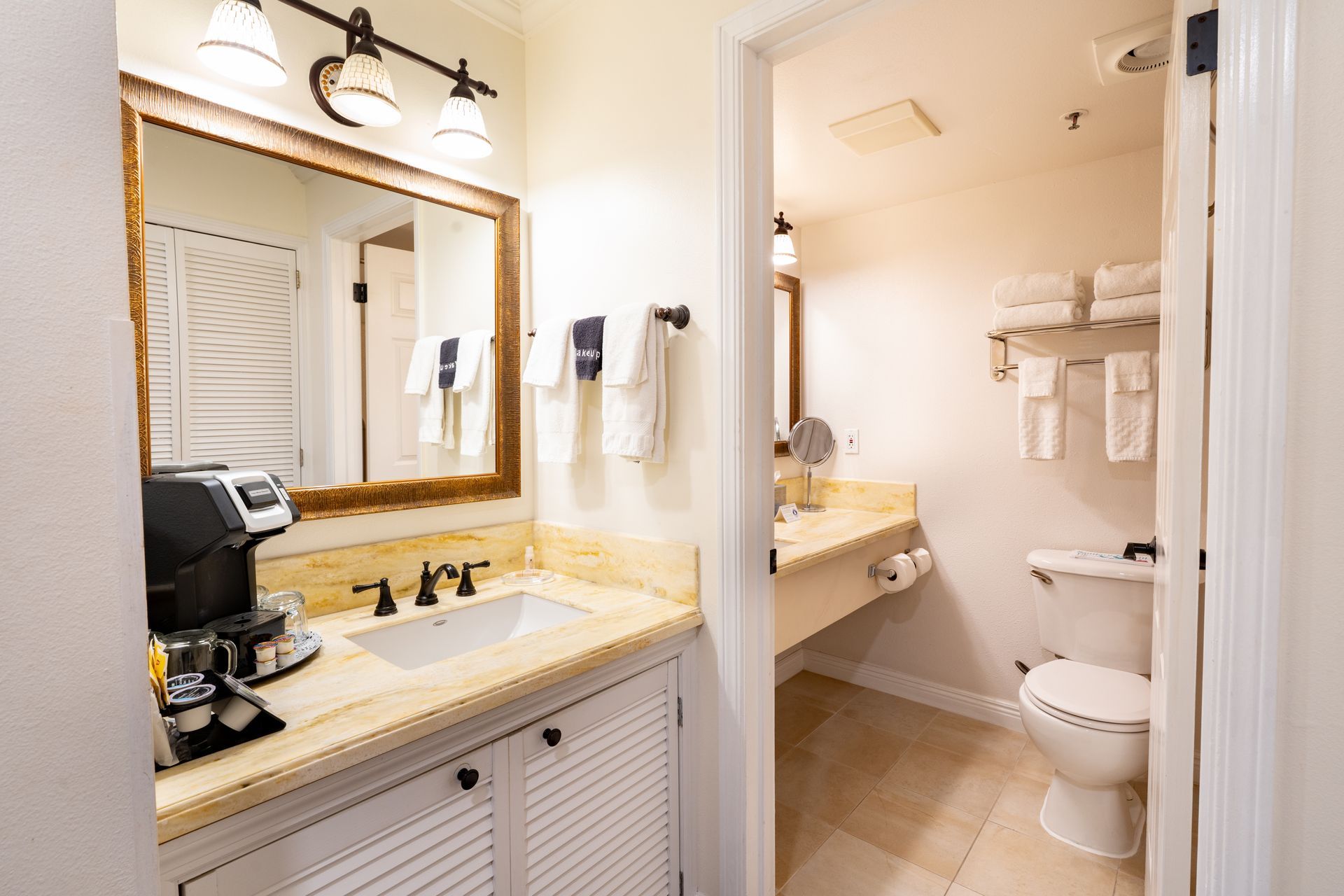Bathroom with sink, mirror, and toilet. Light-colored countertop and walls. Doorway to another bathroom area.