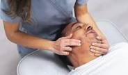 A person receiving a facial massage. A health professional is seen with hands on the patient's face.