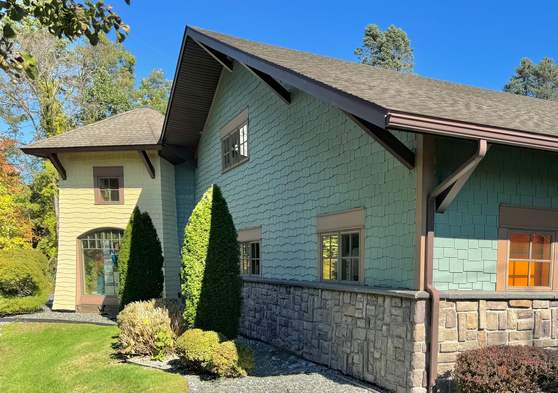 Multi-colored house with stone and green siding, brown trim, and a blue sky.