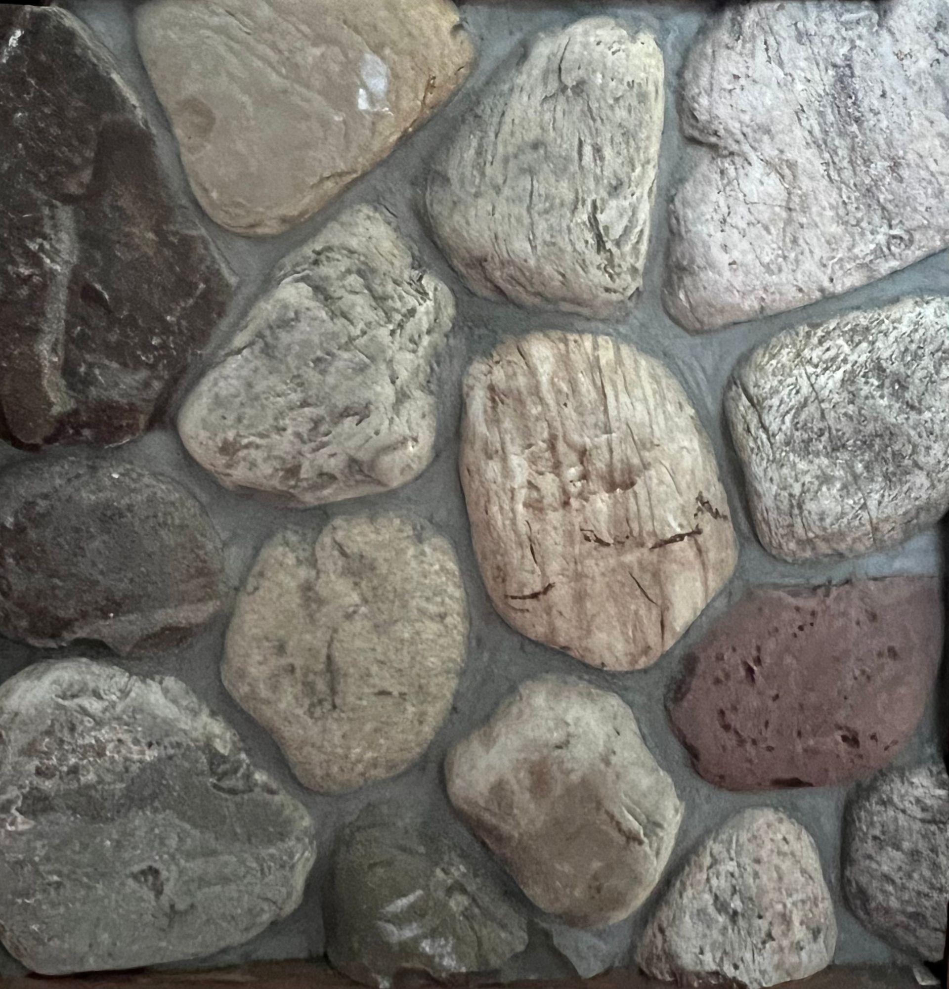A stone wall with a lot of different colored round rocks