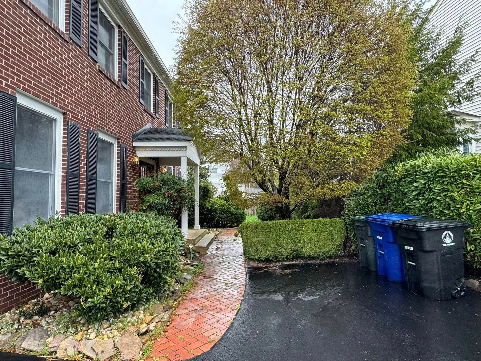 A brick house with a driveway and trash cans in front of it.