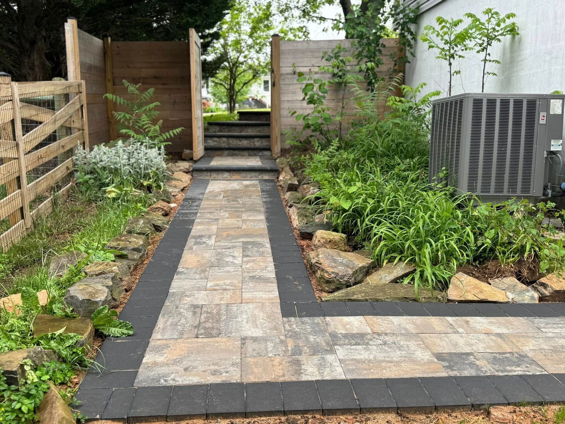 A brick walkway leading to a house with a wooden fence.