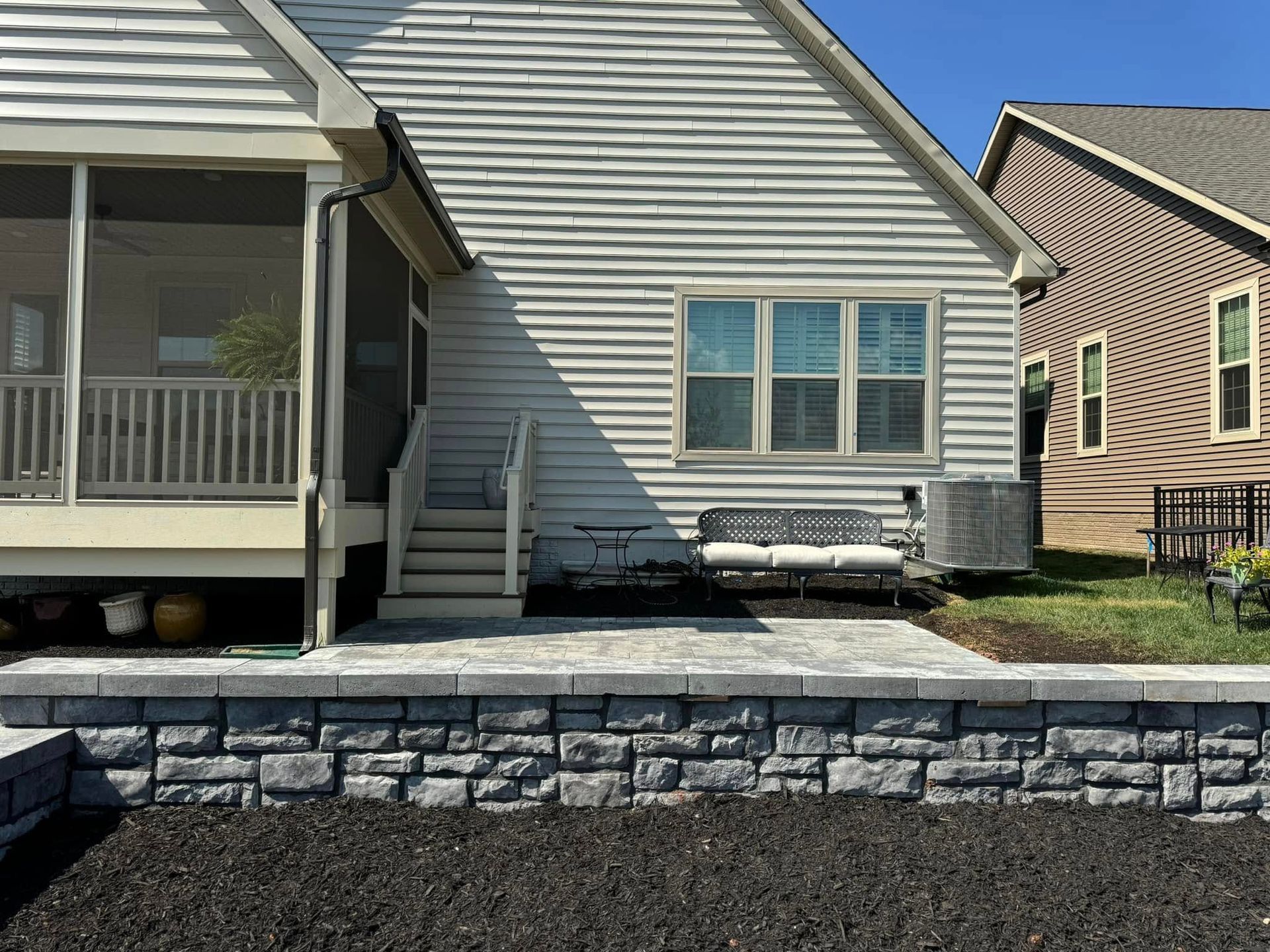 A white house with a screened in porch and a stone wall in front of it.