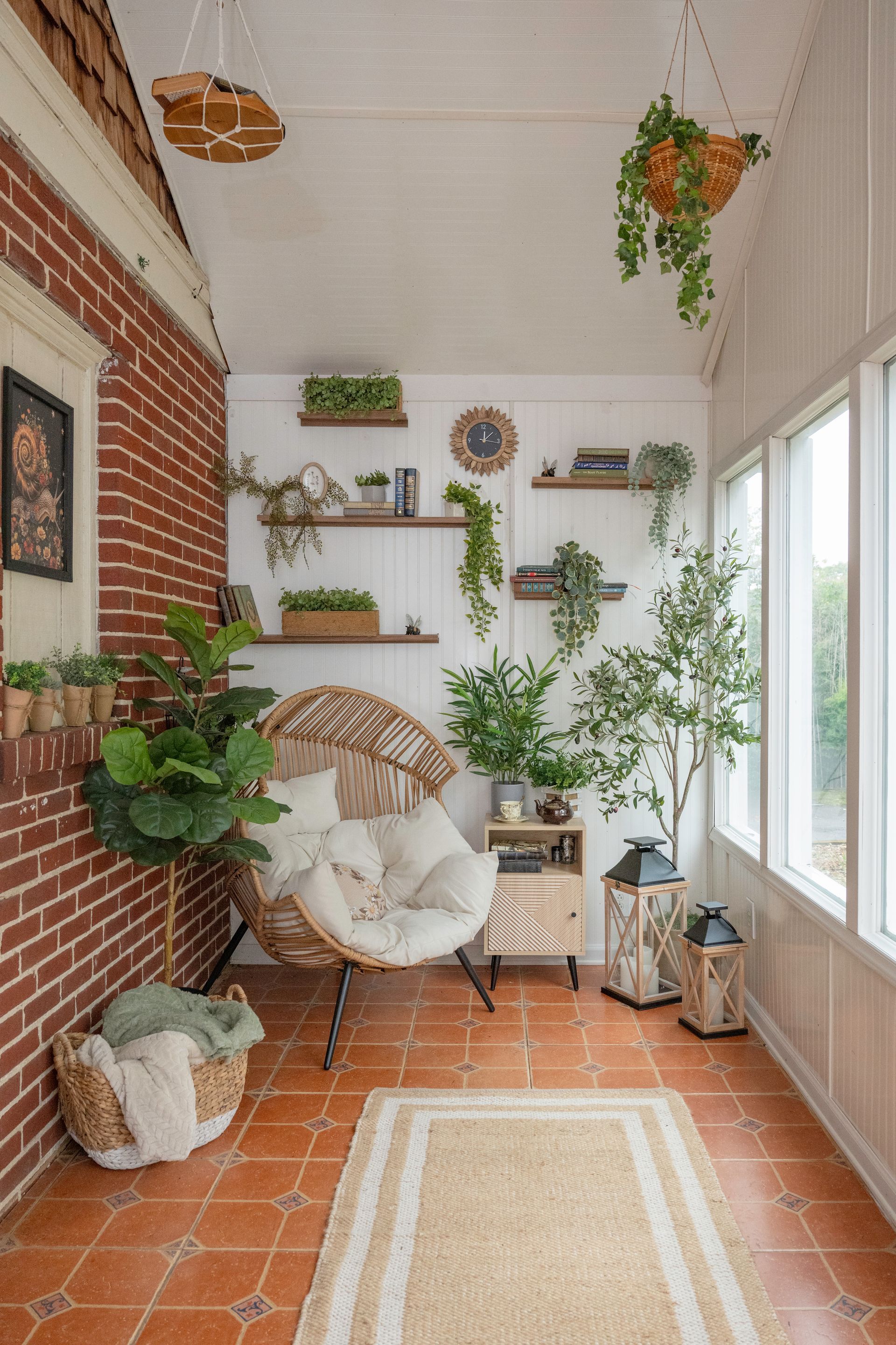 Sunroom with brick wall, rattan chair, plants, shelves, and terracotta tile floor.