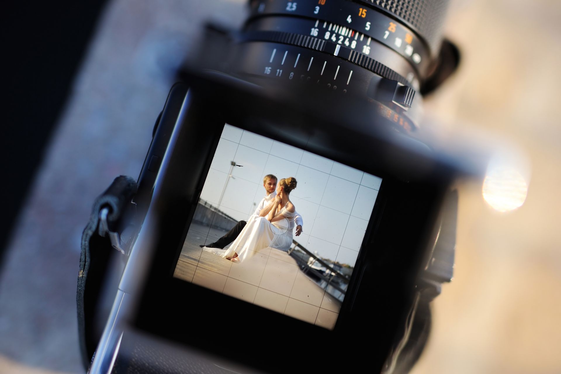 Viewfinder of a camera displaying a photo of a bride and groom embracing outdoors on a sunny day.