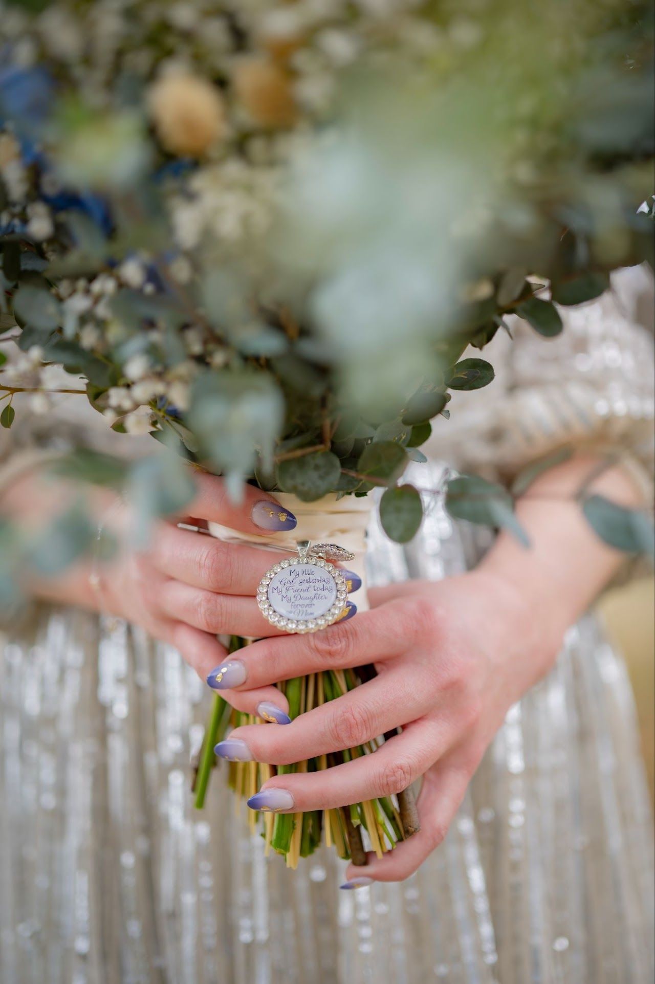 Person holding a bouquet of flowers. Hands with blue/purple nails, ivory ribbon, sparkly dress.