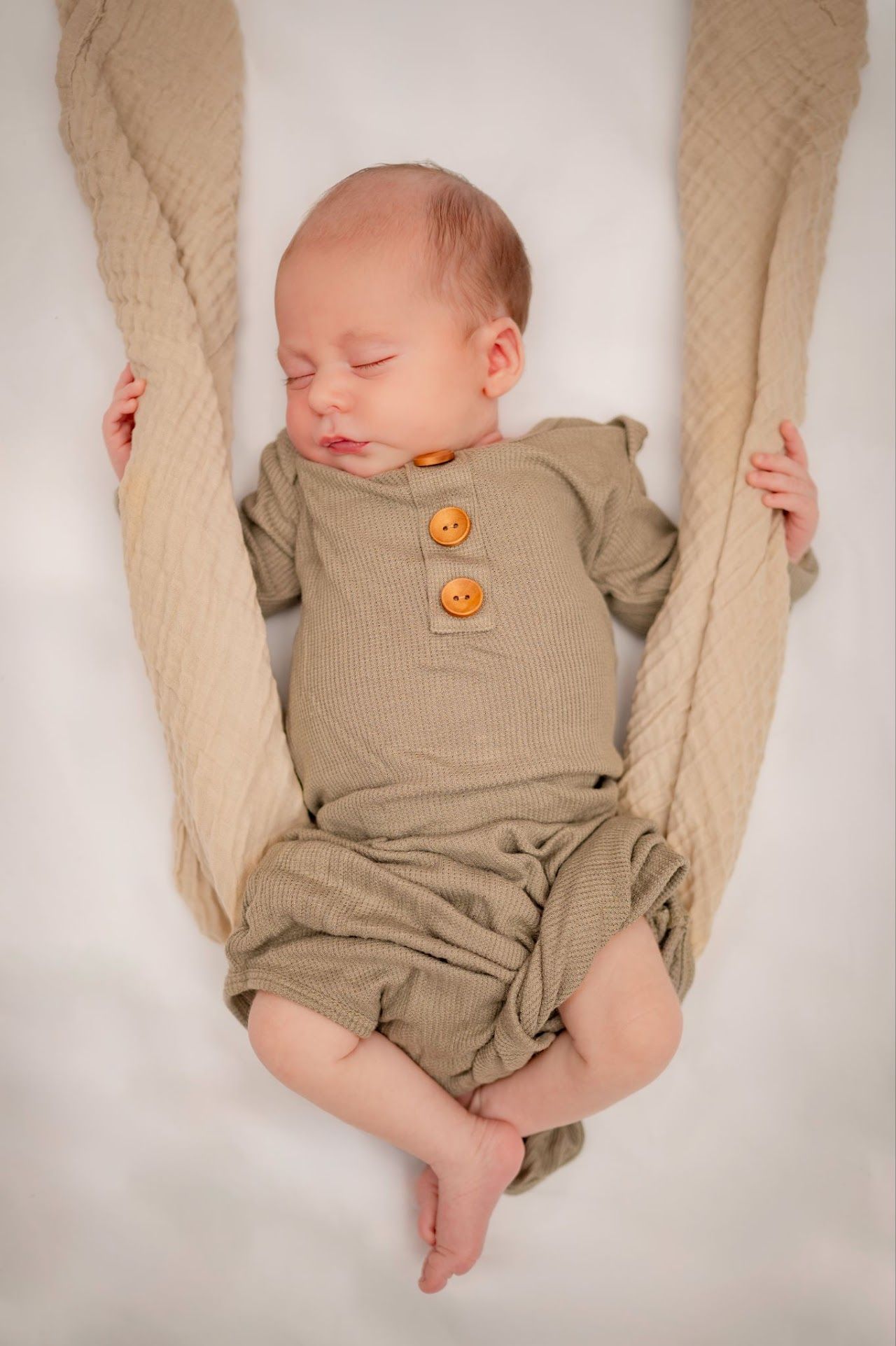 Newborn baby sleeping in a beige knitted outfit, suspended by a blanket.