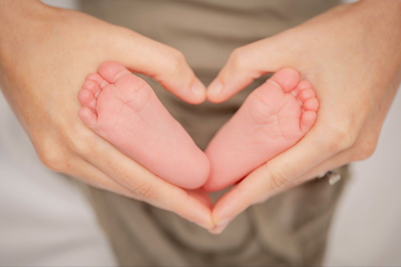Hands forming a heart around a baby's tiny pink feet.