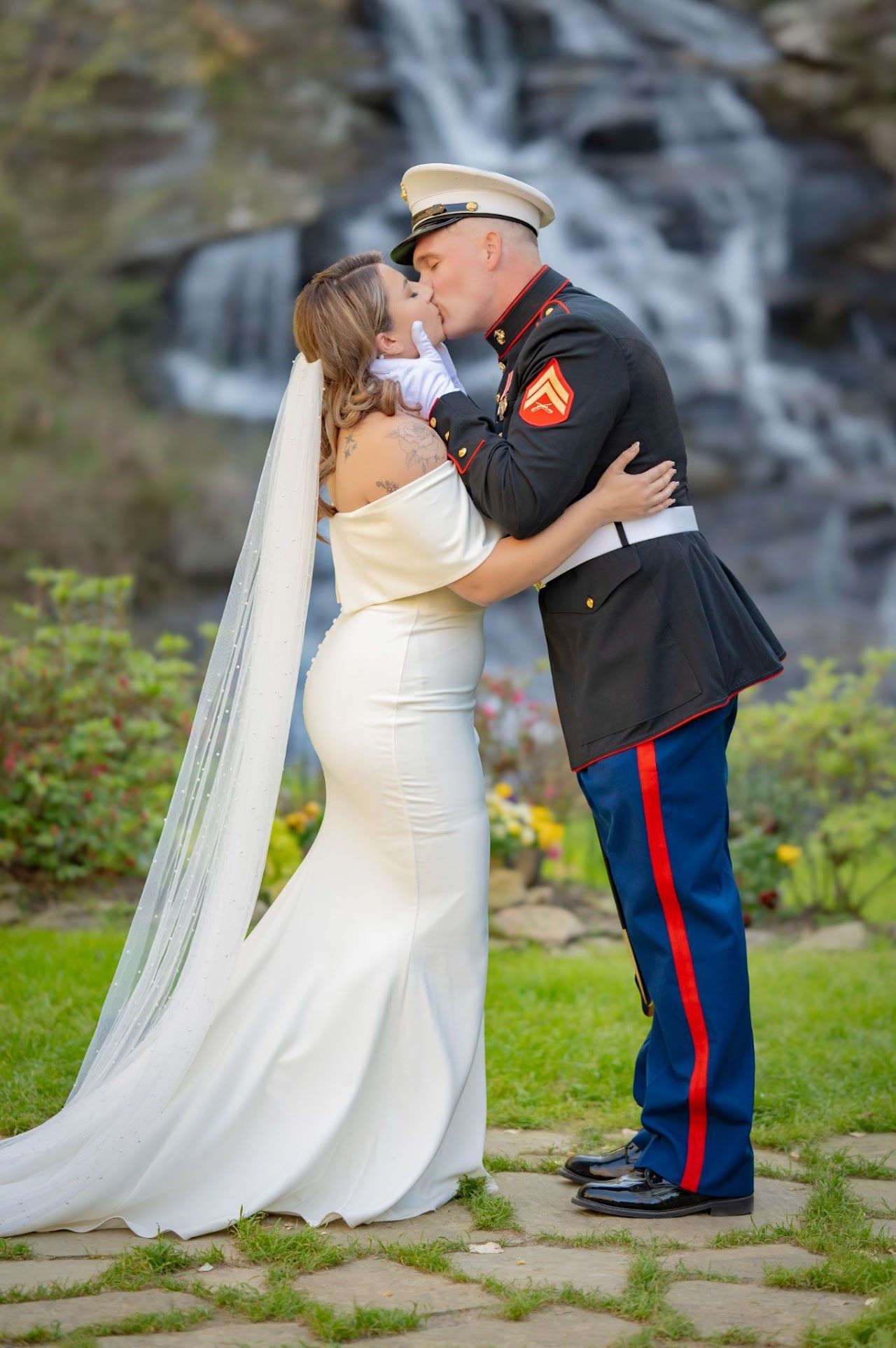 Bride and Marine in uniform kiss near waterfall. The bride wears a white gown, Marine in dress blues.