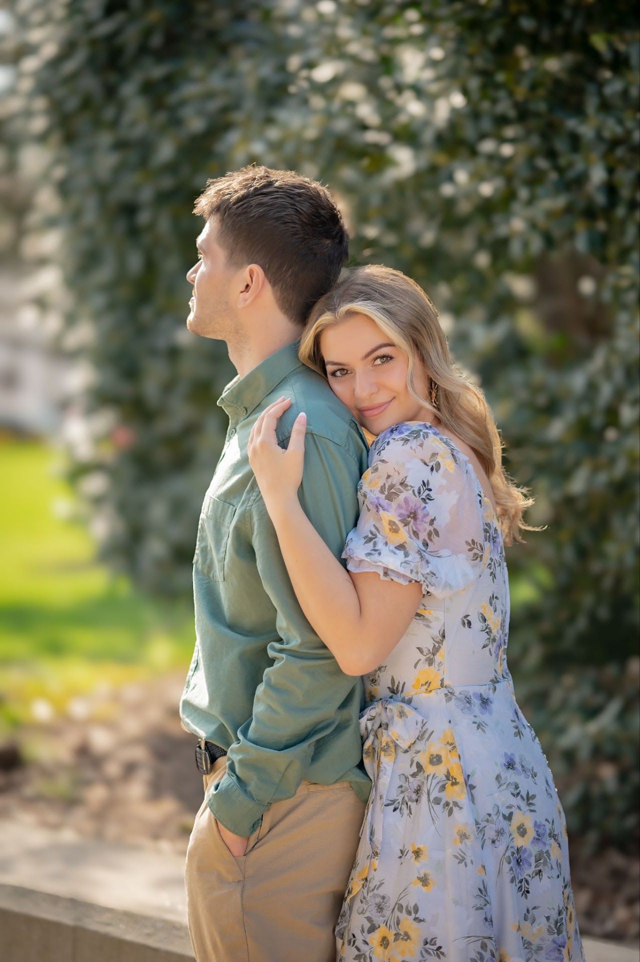 Woman in floral dress hugs man in green shirt; sunny outdoor setting.