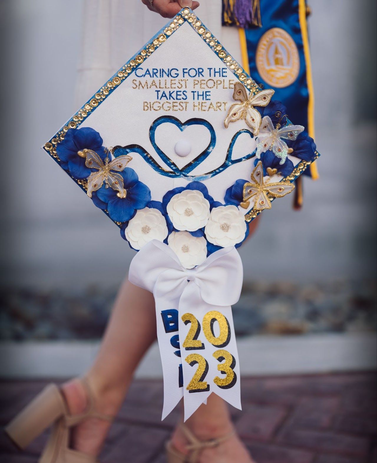 Graduation cap with blue flowers, a stethoscope heart design, and 