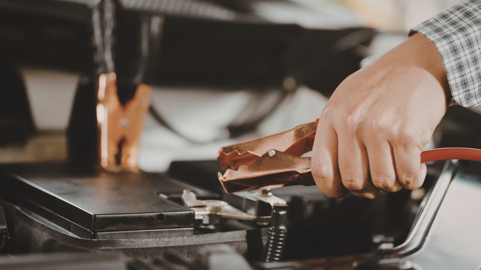 Hand connecting jumper cable to car battery.