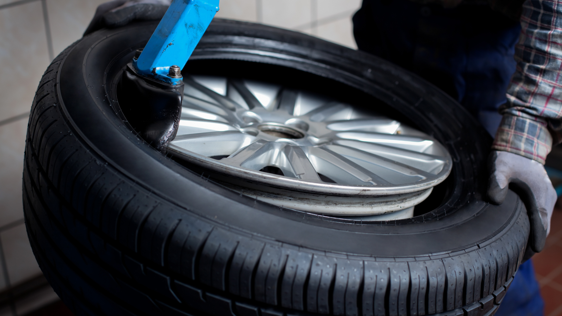 Tire being removed from a wheel rim with a machine by a person wearing work gloves.